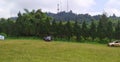 Two cars are parked in a large green grass field and green trees