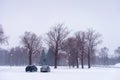 Two cars parked next to a park during snowstorm, winter scene, copy space Royalty Free Stock Photo