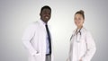 Two caucasian and afro american smiling doctors standing looking in to camera on gradient background. Royalty Free Stock Photo