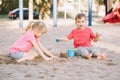 Two Caucasian children sitting in sandbox playing with beach toys. Little girl and boy friends having fun together on playground. Royalty Free Stock Photo