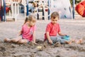 Two Caucasian children sitting in sandbox playing with beach toys. Little girl and boy friends having fun together on playground. Royalty Free Stock Photo