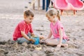 Two Caucasian children sitting in sandbox playing with beach toys. Little girl and boy friends having fun together on playground. Royalty Free Stock Photo