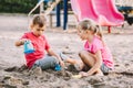 Two Caucasian children sitting in sandbox playing with beach toys. Little girl and boy friends having fun together on playground. Royalty Free Stock Photo