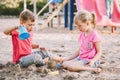 Two Caucasian children sitting in sandbox playing with beach toys. Little girl and boy friends having fun together on a playground Royalty Free Stock Photo