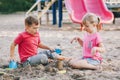 Two Caucasian children sitting in sandbox playing with beach toys. Little girl and boy friends having fun together on playground. Royalty Free Stock Photo