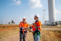 Two Caucasian engineers or technicians shake hands and stay in front of cluster of windmill or wind turbine after success the