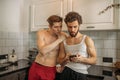 Two gays look at smartphone, in kitchen