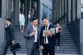 Two Caucasian handsome businessmen in suits and ties holding coffee in hands and walking from office building after work Royalty Free Stock Photo