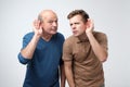 Two caucasian men hearing with hand on ear isolated on a white background. Please speak loudly. Royalty Free Stock Photo