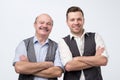 Two caucasian men, a mature adult around 30 years and a senior standing with folded hands and smiling Royalty Free Stock Photo