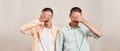 Two caucasian men, twin brothers covering eyes with hand while posing together isolated over beige background, panoramic