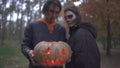 Two caucasian people in Halloween costumes with horrifying make-up looking in the camera in the autumn park. Serious