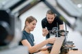 Two Caucasian professional technician or engineer workers sit in workplace and help to check and maintenance small robotic machine Royalty Free Stock Photo