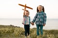 two Caucasian sisters or girlfriends are walking in the field, playing and launching a toy plane. Children in plaid