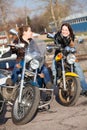 Two Caucasian women motorcyclists talk incessantly while sitting face-to-face on their motorcycles, spring season
