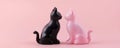 Two ceramic cat figurines, black and pink, facing each other on a pastel pink background. Decorative objects and home Royalty Free Stock Photo