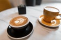 Two ceramic cups with cappuccino and with latte on a wooden table in a coffee shop. Latte with a beautiful foam with a flower Royalty Free Stock Photo