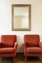 Two chairs and golden framed mirror on a white wall with soft natural light coming in from outside. beauty Royalty Free Stock Photo