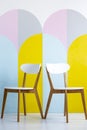 Two chairs set on a patterned wall with yellow accents in bright