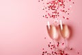 Two champagne glasses making a toast with a burst of red heart-shaped confetti, set against a pink background Royalty Free Stock Photo