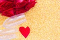 Two champagne glasses, a red bouquet of roses and a heart of petals lies on the side on a bright gold background. top