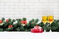 Two champagne glasses setting next to a red gift box on snowy ta