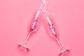 Two champagne glasses with splash of pink stars shaped confetti over pink background. Top view. Valentine`s Day concept