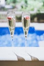 Two champagne glasses with strawberry on sunny terrace outdoor patio overlooking swimming pool at summer day outside of Royalty Free Stock Photo