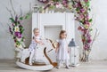 Two charming little girls play in the light room decorated with flowers. Baby girl swinging on a wooden horse Royalty Free Stock Photo