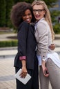 Two charming multi race businesswomen are happily hugging and smiling in park. Royalty Free Stock Photo