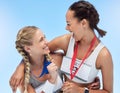 Two cheerful athletic women embracing while holding gold medals from competing in sports event. Joyful fit active