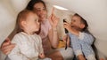 Two cheerful boys having fun with young mother under blanket and playing with flashlight. Family having time together, parenting, Royalty Free Stock Photo