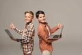 Two cheerful brothers holding laptops, showing thumbs up and looking at camera Royalty Free Stock Photo