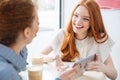 Two cheerful charming young woman using tablet in cafe