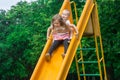 Two cheerful children roll down the yellow slide on the playground and scream at an exciting speed.