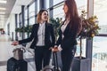 Two cheerful female friends waiting for a plane standing in airport hall with heavy luggage near the gates Royalty Free Stock Photo