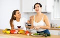 Two cheerful female roommates drinking wine and preparing dinner at home