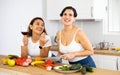 Two cheerful female roommates drinking wine and preparing dinner at home