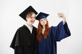 Two cheerful graduates of university fooling making selfie over white background.