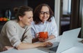 Two cheerful happy women, adult daughter with elderly mother looking at laptop screen at home