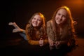 Two cheerful joyfull sisters having fun together in dark studio with black background