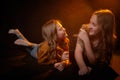 Two cheerful joyfull sisters having fun together in dark studio with black background