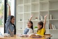Two cheerful little Asian girls and a kind female teacher are raising their hands Royalty Free Stock Photo