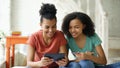 Two cheerful mixed race curly girlfriends shopping online with tablet computer and credit card at home Royalty Free Stock Photo