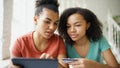 Two cheerful mixed race curly girlfriends shopping online with tablet computer and credit card at home Royalty Free Stock Photo