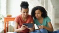 Two cheerful mixed race curly girlfriends shopping online with tablet computer and credit card at home Royalty Free Stock Photo