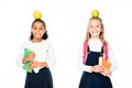 two cheerful multicultural schoolgirls with apples on heads holding books isolated on white. Royalty Free Stock Photo