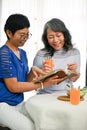 Two cheerful retired Asian women enjoy reading a book while having a healthy brunch together Royalty Free Stock Photo
