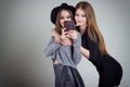 Two cheerful smiling girl girlfriends photographed on the phone, do selfie phone in the studio on a gray background Royalty Free Stock Photo