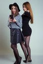 Two cheerful smiling girl girlfriends photographed on the phone, do selfie phone in the studio on a gray background Royalty Free Stock Photo